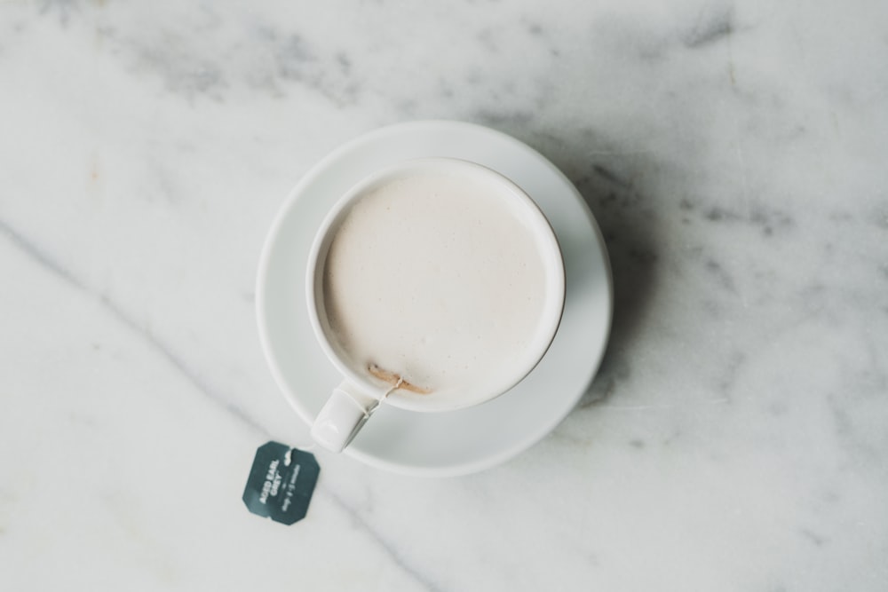 Milch auf weißem Keramikbecher auf weißer Untertasse auf weißer Oberfläche