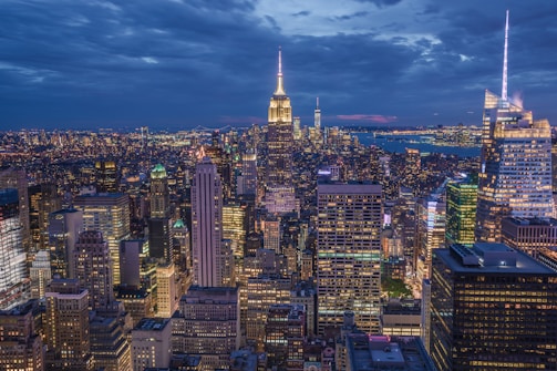 A vibrant cityscape at dusk with glowing lights and deep shadows.