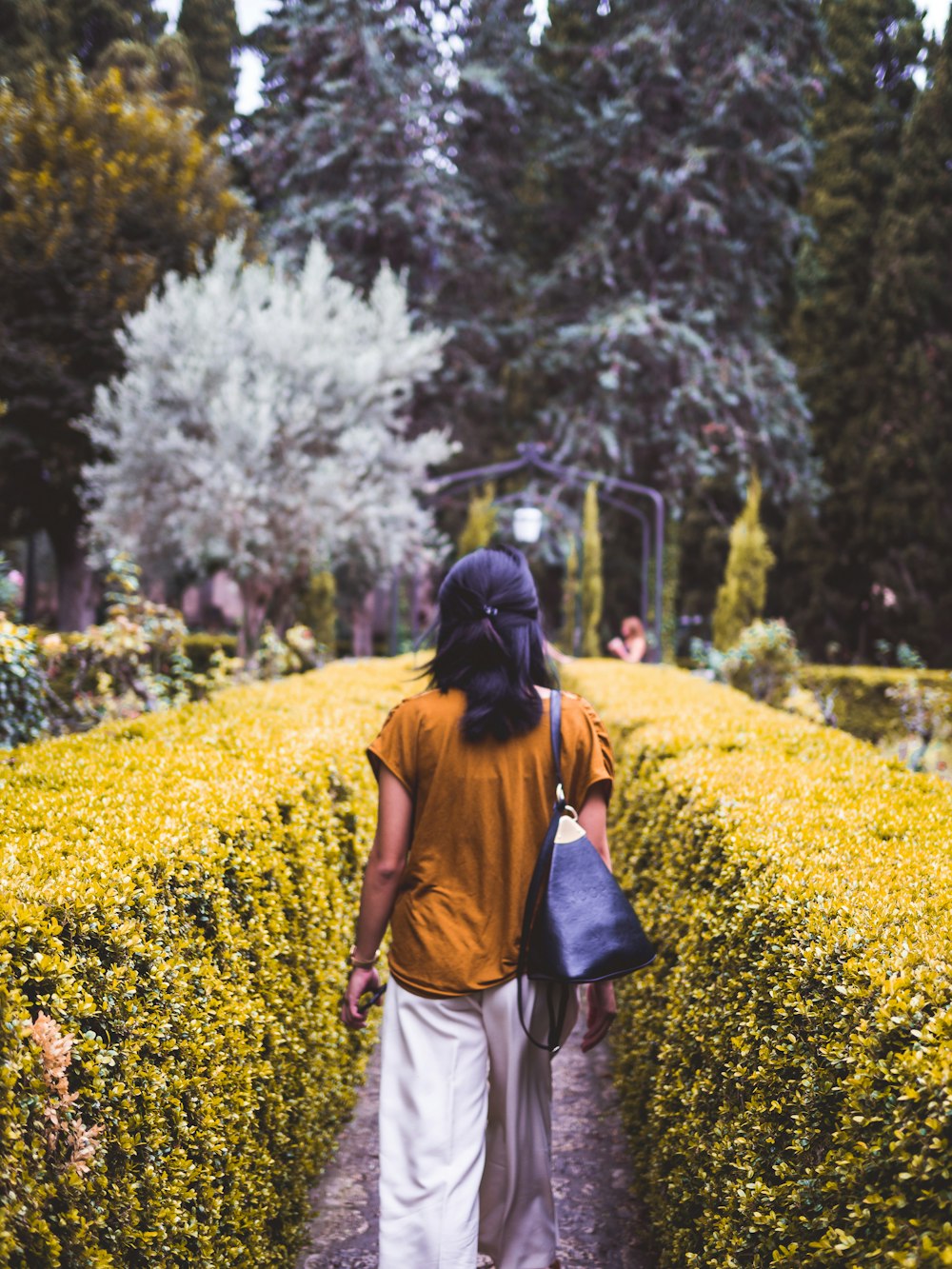 woman walking between green bushes during daytime