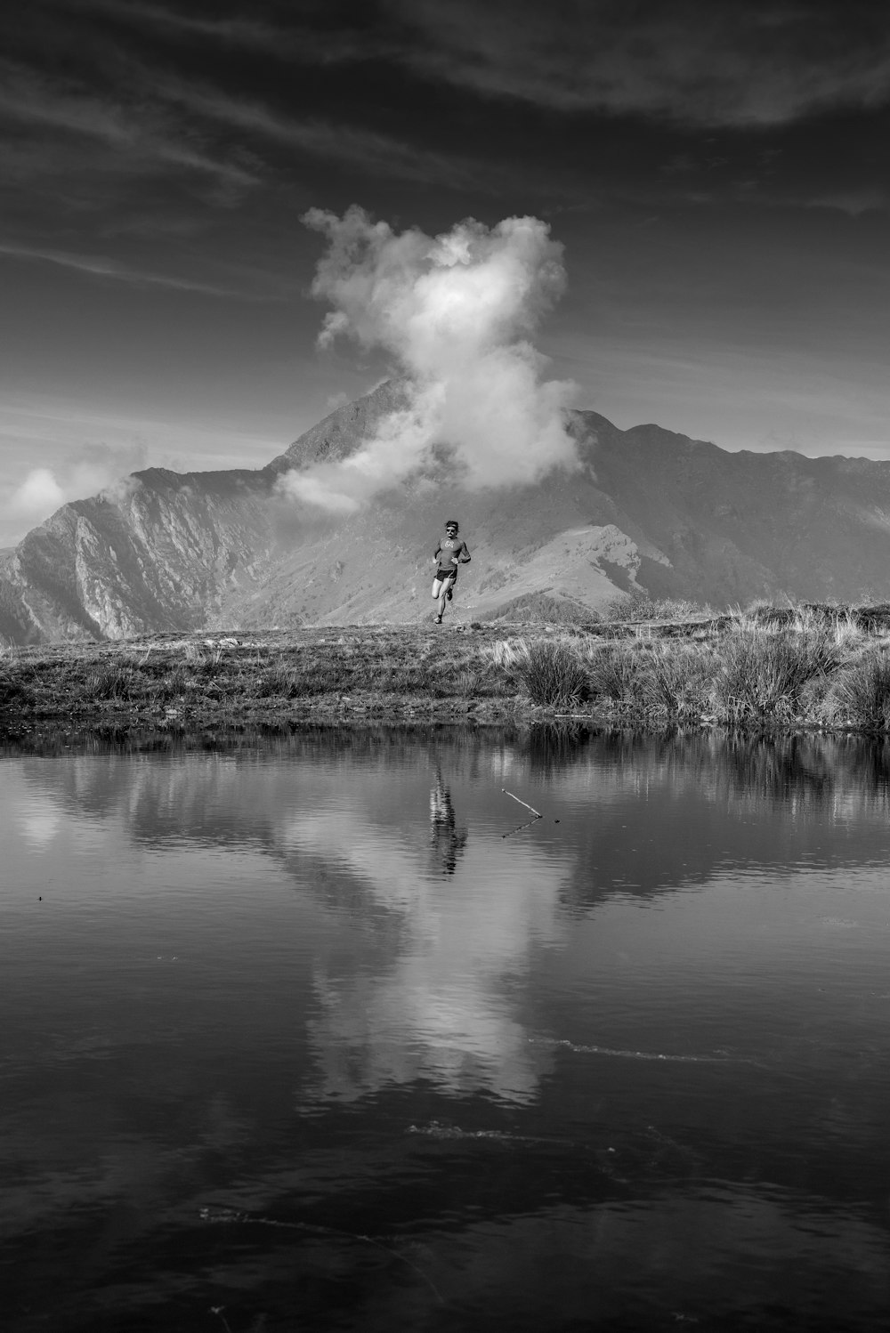 grayscale photo of man jump over calm body of water