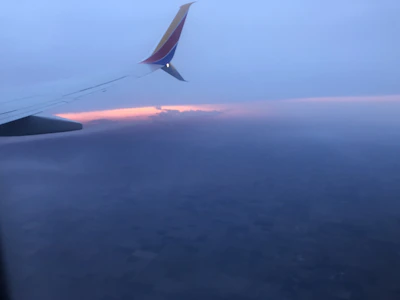 An airplane soaring above clouds with a vibrant sunset backdrop.