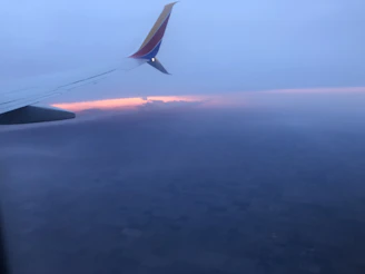 Dramatic clouds glowing with hues of pink and purple as dusk falls behind an airplane wing.