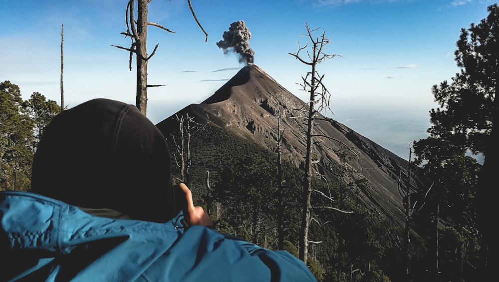 man standing near withered tree facing mountain