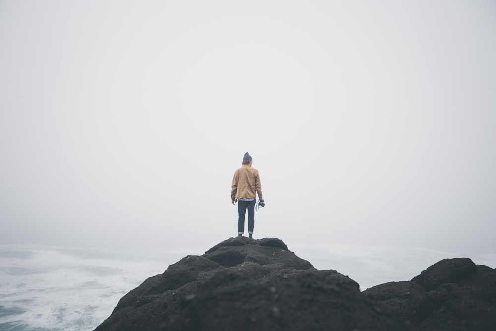 man standing on rocky mountain under white sky during daytime