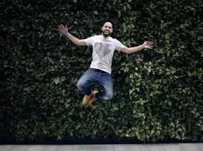 man wearing t-shirt and jeans jumpshot in front of a green hedge