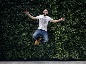 man wearing t-shirt and jeans jumpshot in front of a green hedge