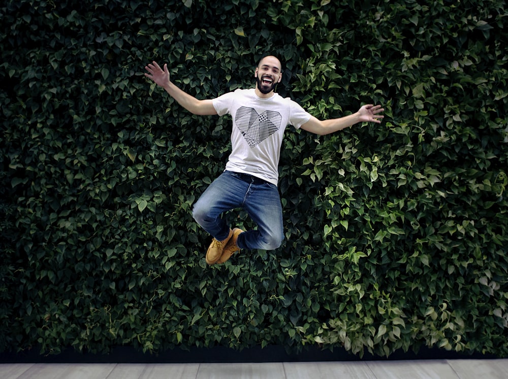 homme portant un t-shirt et un jean jumpshot devant une haie verte