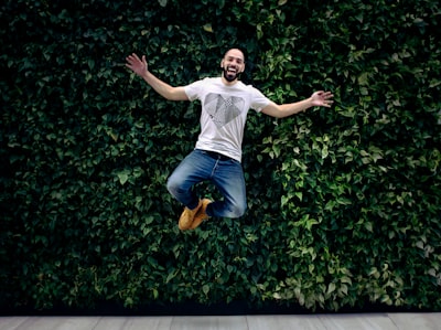 man wearing t-shirt and jeans jumpshot in front of a green hedge energetic teams background