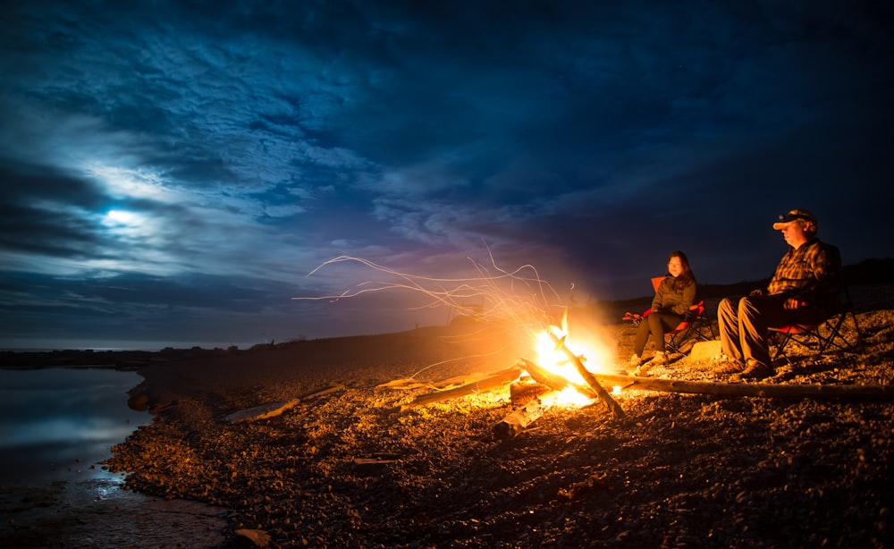 man and woman standing near bonfire on seashore during night