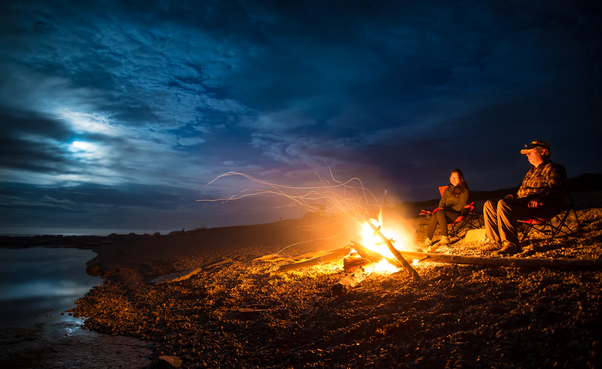 Two campers beside an oceanside campfire at night