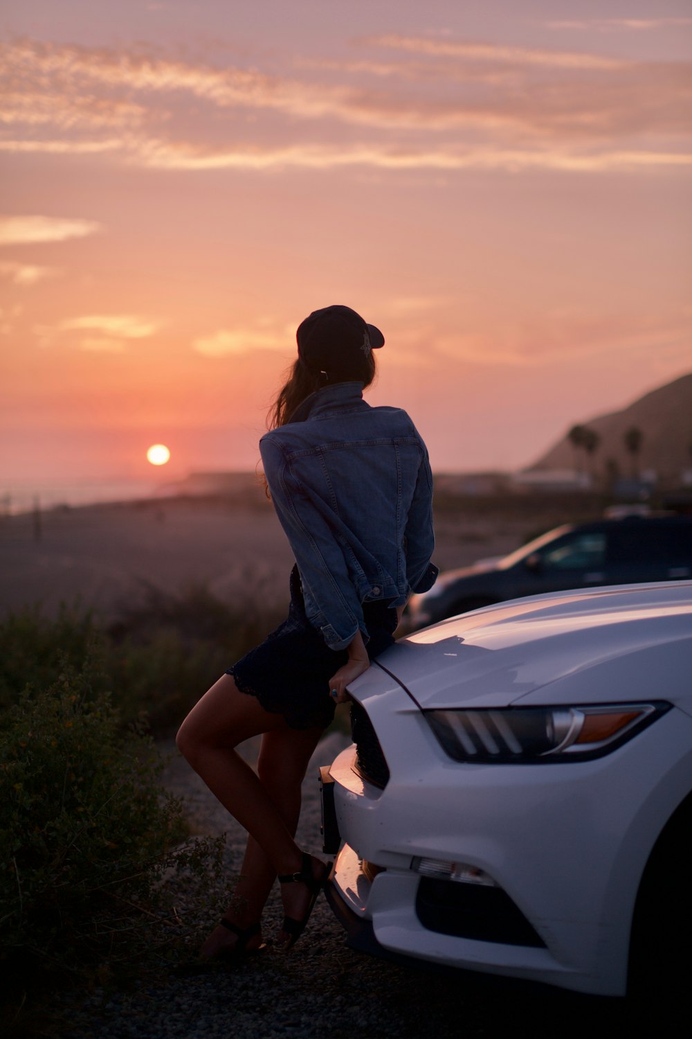 woman leaning on white Ford Mustang GT coupe front bumper during golden hour