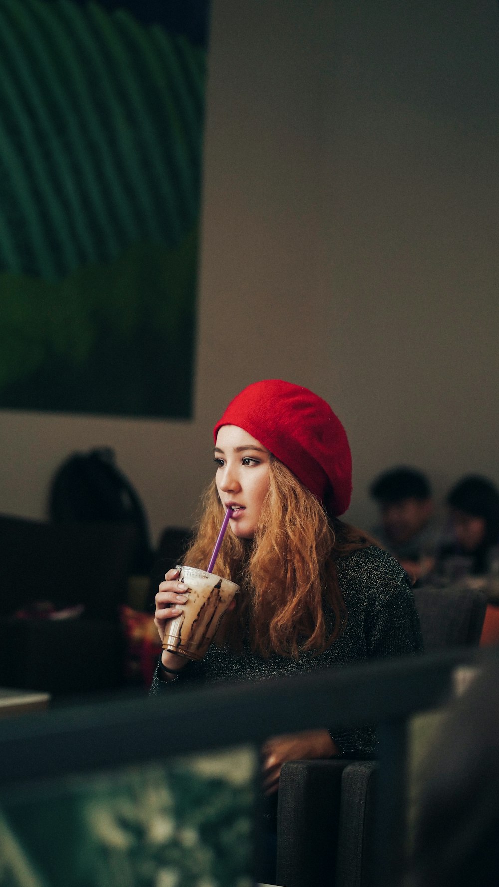검은 재킷과 빨간 니트 모자를 쓰고 일회용 솔로 컵에 음료를 들고 있는 여자