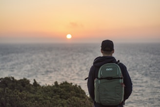 A mature traveler adjusting a backpack strap while overlooking a coastal sunset.
