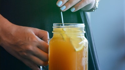 person holding glass mason jar with handle with drink and straw