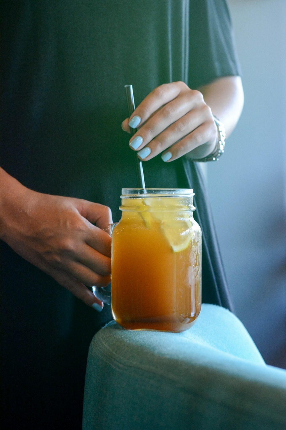 person holding glass mason jar with handle with drink and straw