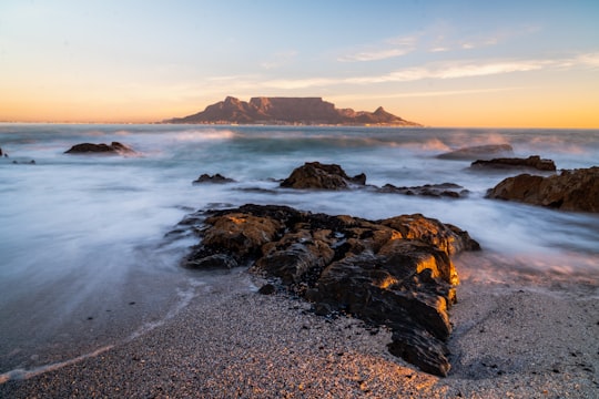 water splashing on shore rocks overlooking island at the horizon in Bloubergstrand South Africa