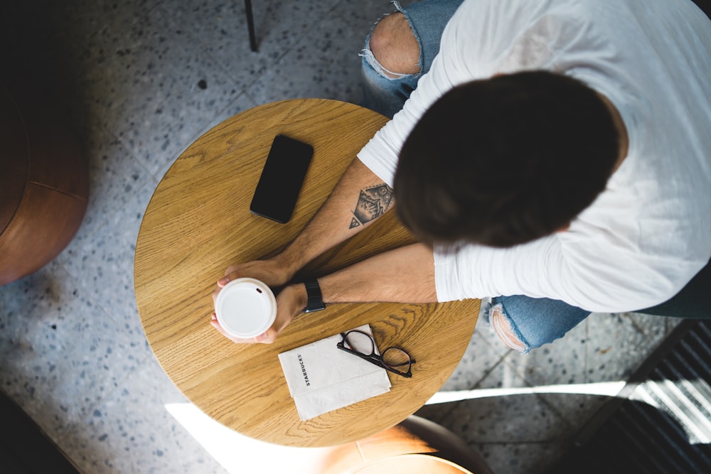 person sitting while holding white cup on brown wooden table