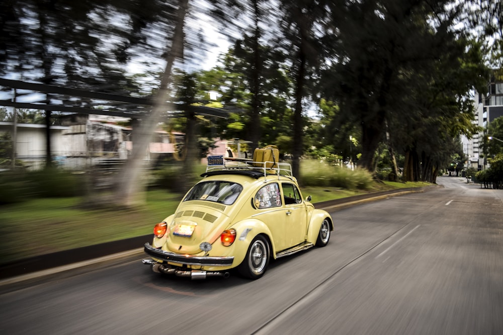 time lapse photo of running yellow Volkswagen Beetle coupe on road