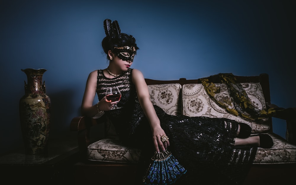 woman with masquerade mask reclining on sofa with glass of wine