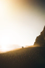 A cinematic shot of a couple walking hand-in-hand along a sandy beach at golden hour.