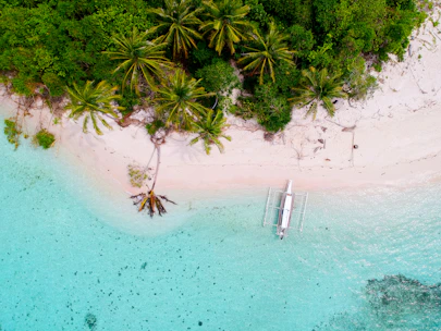 A scenic morning view of a pristine Indonesian beach with emerald-green waters and traditional fishing boats.