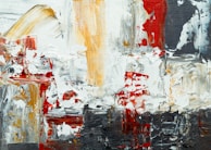 A textured abstract painting with thick, bold brushstrokes in various directions. The artwork features a mix of colors, including red, white, black, and ochre, blending together in a chaotic yet harmonious pattern.