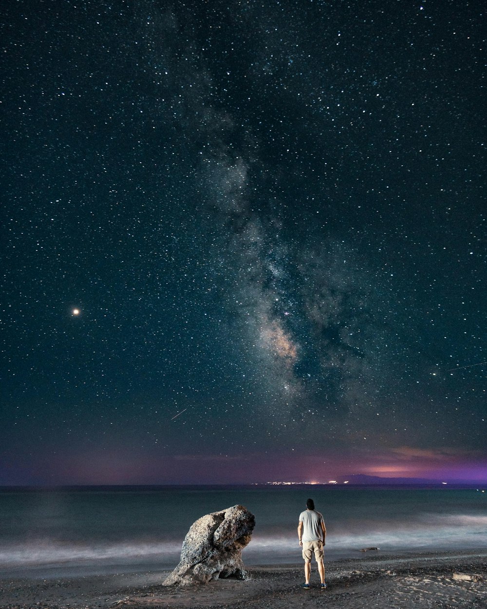 man standing near rock viewing calm sea