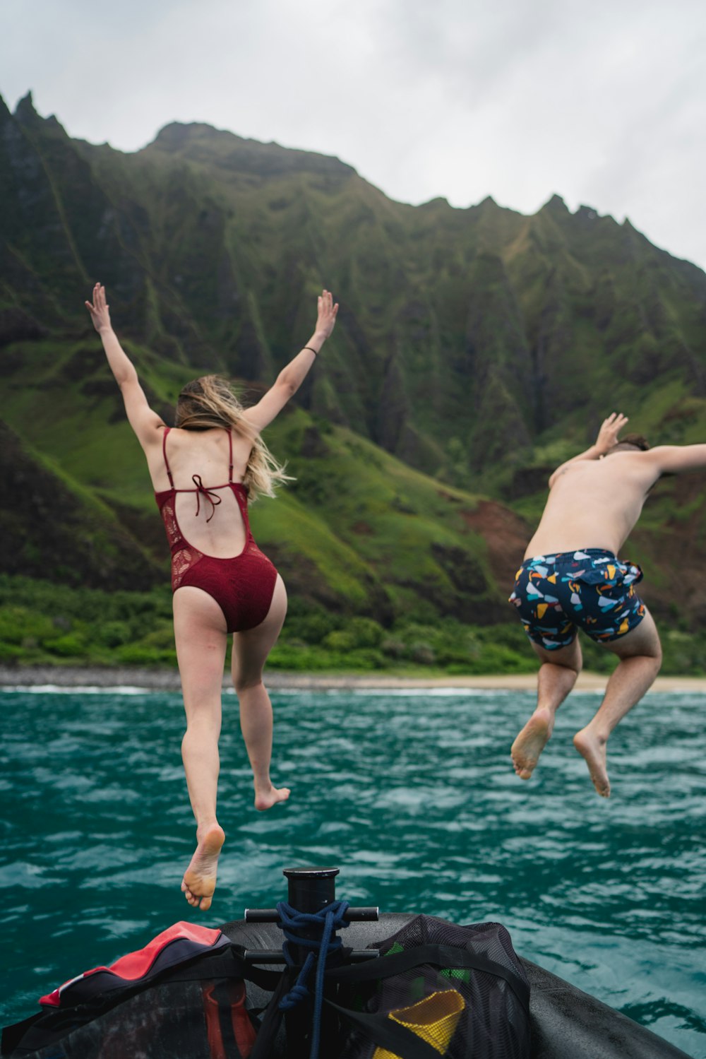 man and woman jumping towards body of water