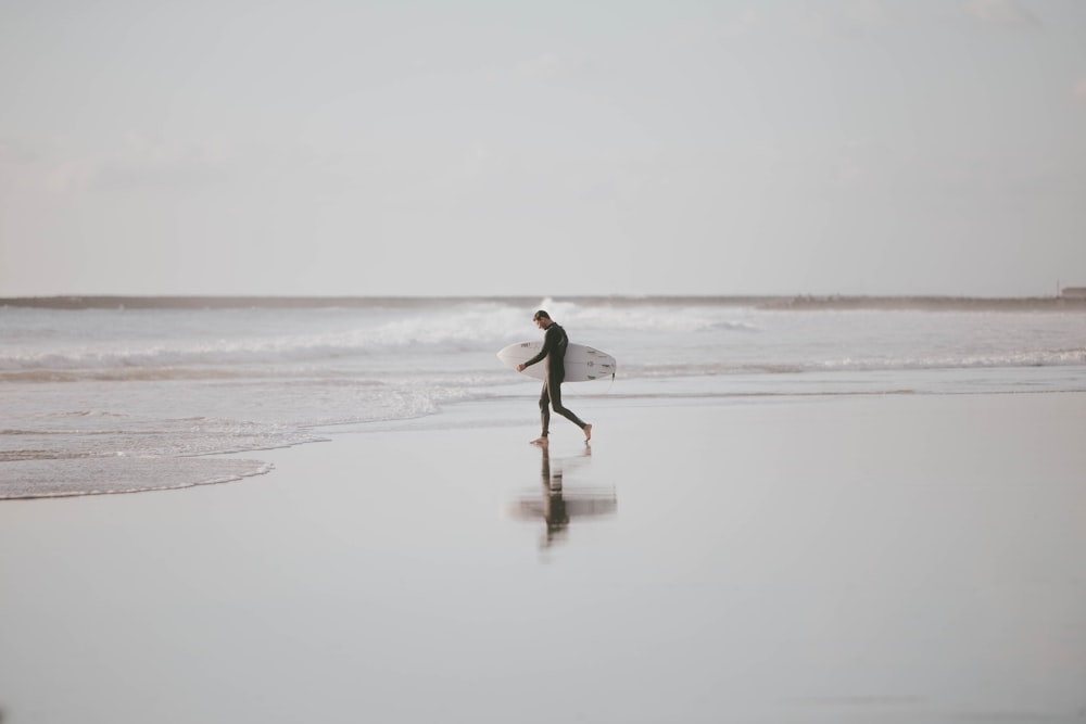 man holding surfboard walking in the beach during daytime