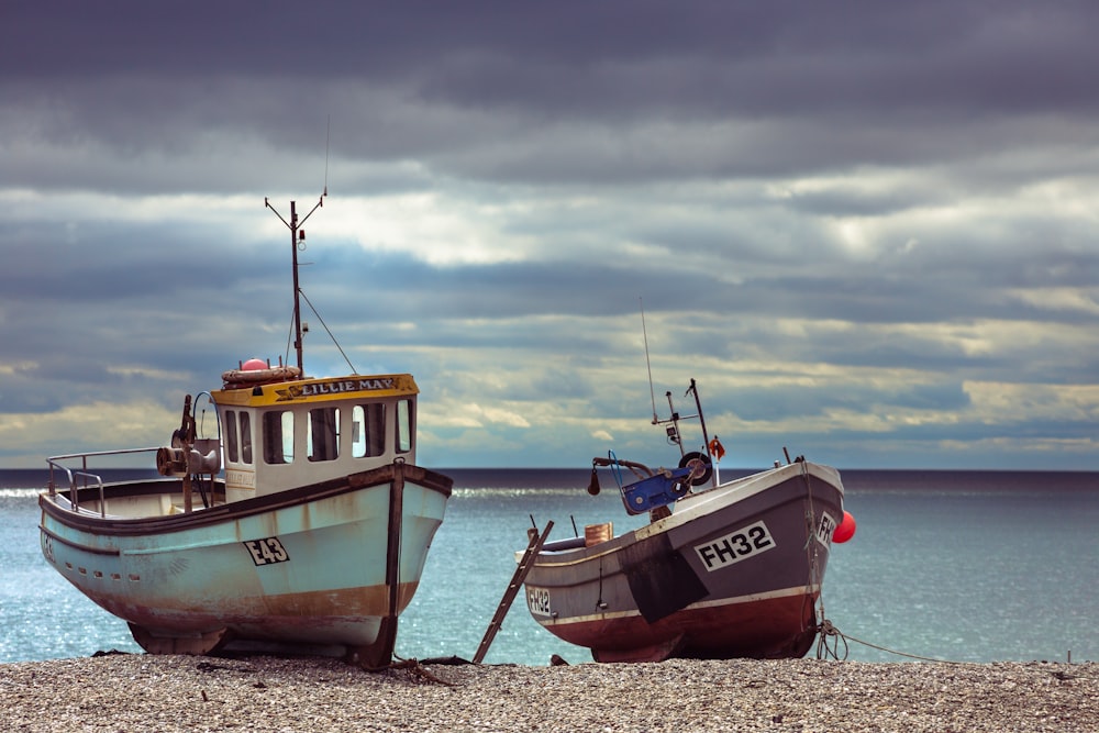 two blue and black boats on seashore under cloudy sky