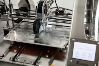 A 3D printer in operation, with a close-up view of the printing head moving over the print bed. The printer's mechanical components and electronic controls are visible, emphasizing precision and technology.