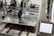 A 3D printer in operation, with a close-up view of the printing head moving over the print bed. The printer's mechanical components and electronic controls are visible, emphasizing precision and technology.
