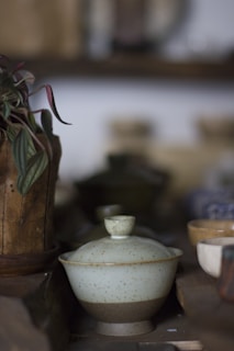 A rustic ceramic mug with a speckled finish resting on a wooden table beside a steaming cup of tea.