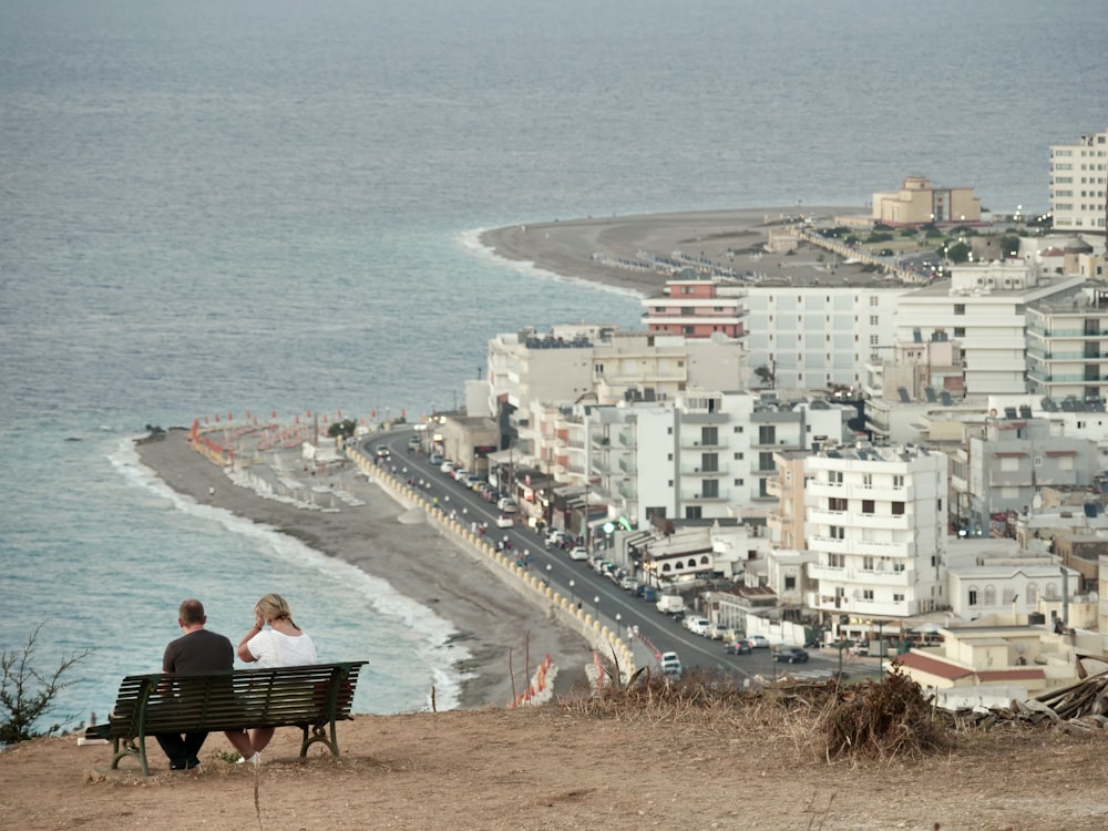 man and woman sitting on bench facing calm sea during daytime