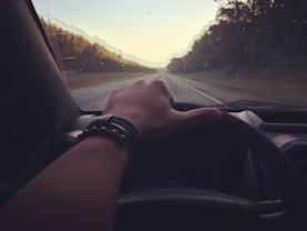 A driver’s hands gripping a classic manual steering wheel on an open road at dusk.