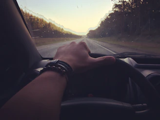 A driver’s hands gripping a classic manual steering wheel on an open road at dusk.