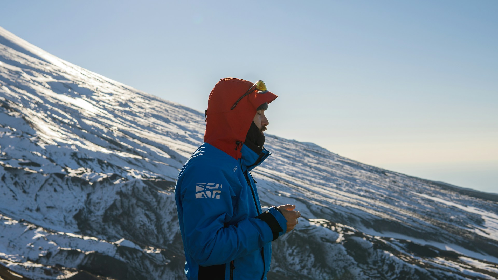 A skier pausing on a snowy slope, bundled in Bright Eye's cozy jacket and beanie, with the crisp mountain air visible in the clear blue sky.