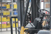Industrial warehouse with technicians working on forklifts surrounded by black and gray machinery.