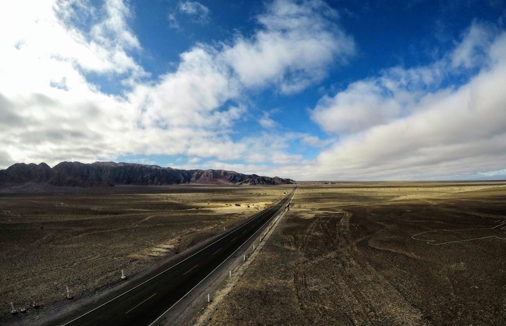 camino entre el desierto bajo nubes blancas durante el día