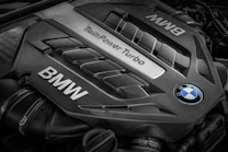A close-up view of a BMW engine cover featuring the words 'TwinPower Turbo' and the BMW logo prominently displayed. The engine components have a sleek, metallic design with visible grooves and contours.