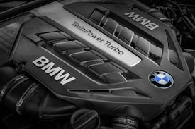 A close-up view of a BMW engine cover featuring the words 'TwinPower Turbo' and the BMW logo prominently displayed. The engine components have a sleek, metallic design with visible grooves and contours.