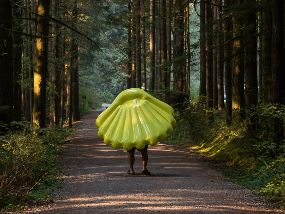 Person mit grünem Muschelhut, die in der Nähe hoher Bäume spazieren geht