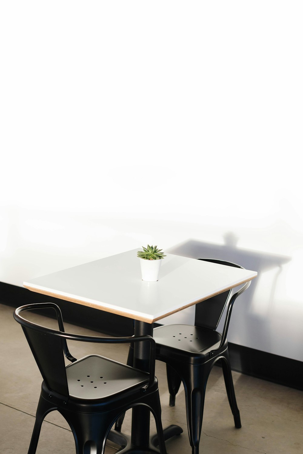 square white wooden table with two black chairs