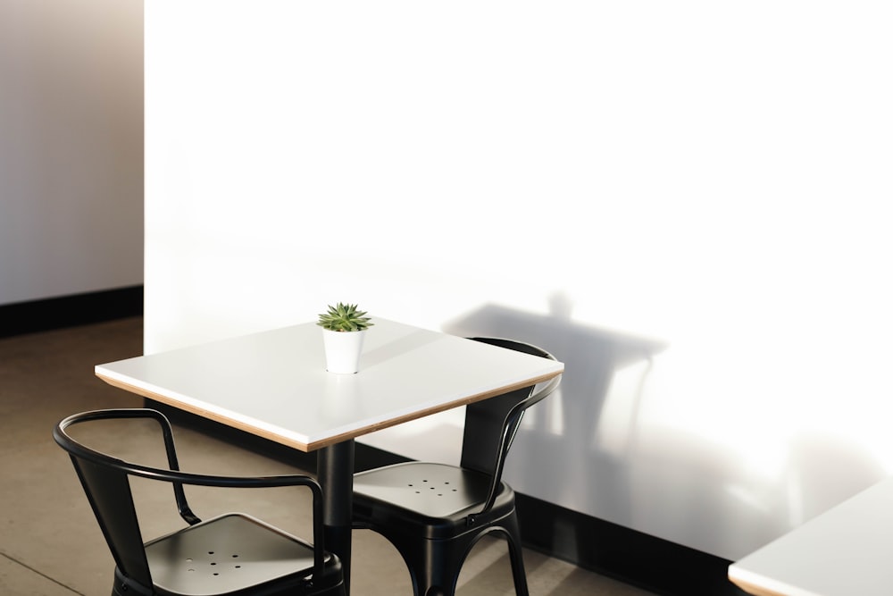 quadratischer weißer Holztisch mit zwei schwarzen Metallstühlen