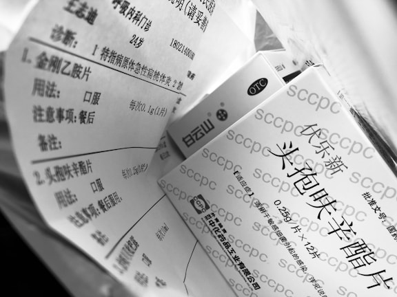 A black and white image shows multiple boxes with Chinese text printed on them, suggesting they are pharmaceutical products. The focus is on the packaging information which includes dosage and usage instructions.