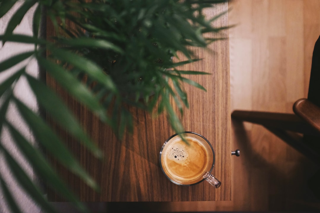 half-filled coffee in clear glass mug beside plant on brown table