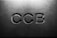 Letters 'CCB' are engraved in a concrete or stone surface, with subtle shadows creating a three-dimensional effect. The lighting is soft, emphasizing the texture of the material.