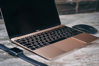 A sleek laptop on a wooden desk with tech gadgets around.