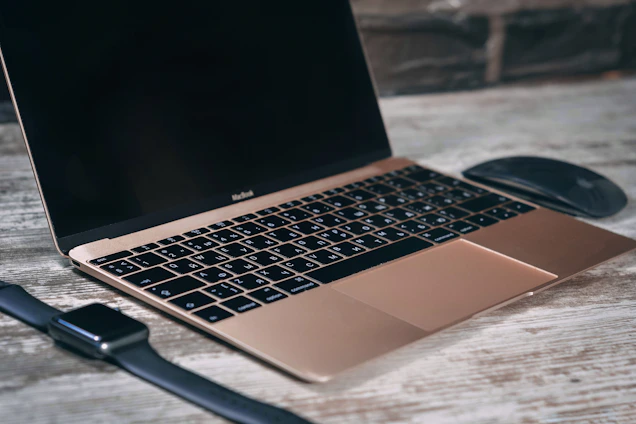 A sleek laptop surrounded by various tech accessories on a clean wooden desk.