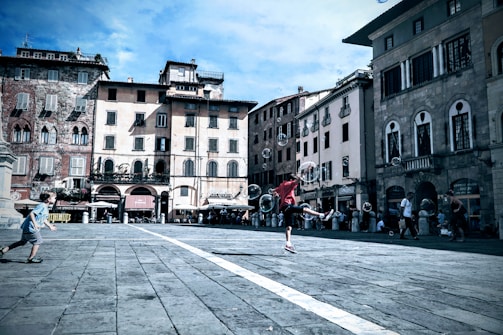 Children playing traditional games in a sunny plaza surrounded by colonial architecture.